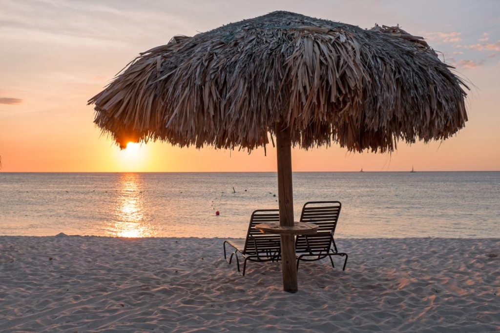 Grass umbrellas at the beach on Aruba island at sunset
